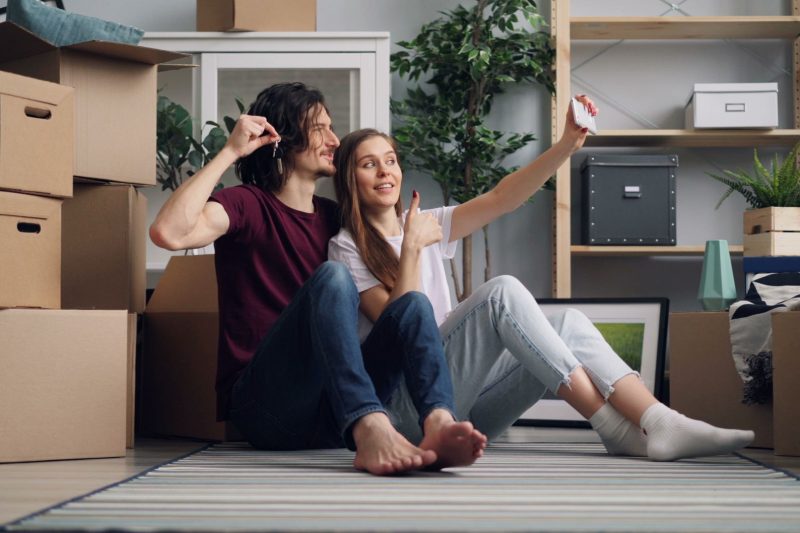 Home 14 Young couple sitting among moving boxes taking a selfie cele 1791306358